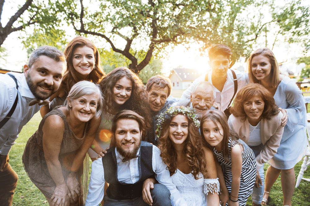A joyful group portrait of a wedding party gathered outdoors, smiling and posing together.